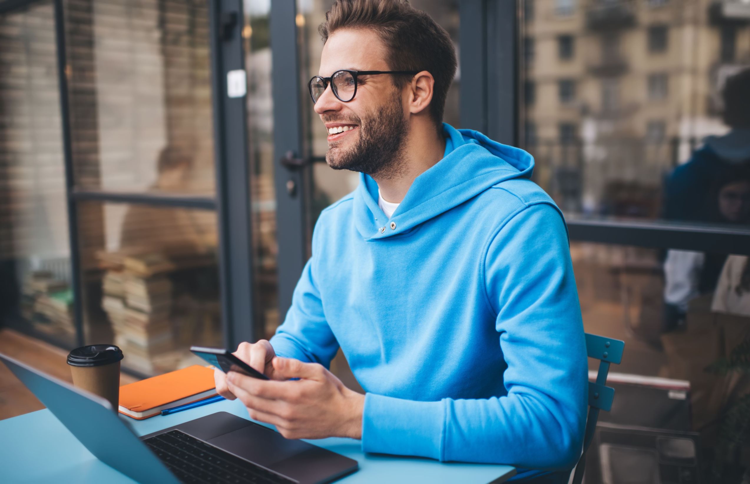 Man smiling whilst holding a mobile phone with a coffee and laptop for number portability or hlr lookup