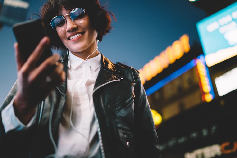Woman holding mobile phone with headphones and sunglasses